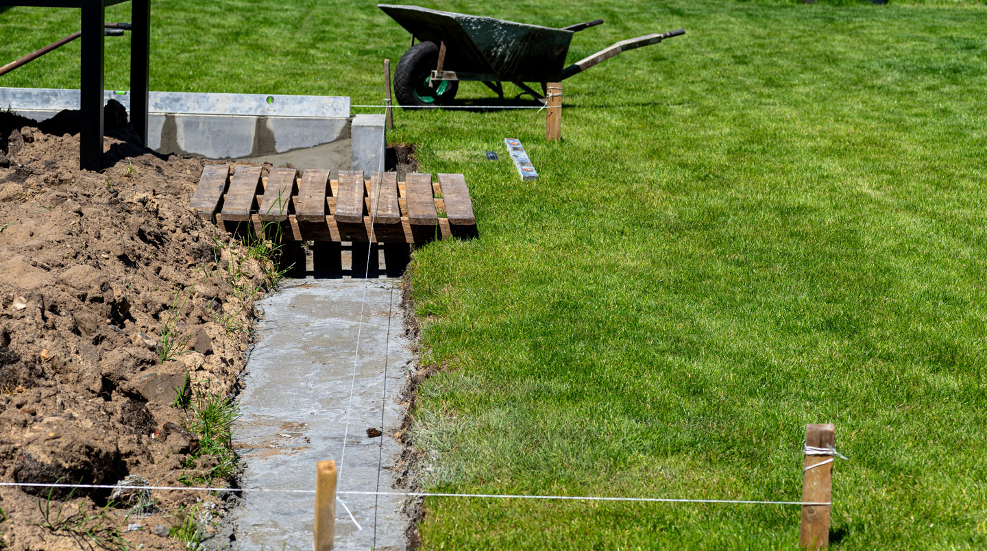 Vue en plongée d'un chantier de patio en construction montrant la structure de solives et un technicien effectuant des mesures de distances avec ses outils professionnels
